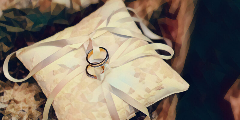 Two wedding rings sitting on top of a pillow with a ribbon over the top